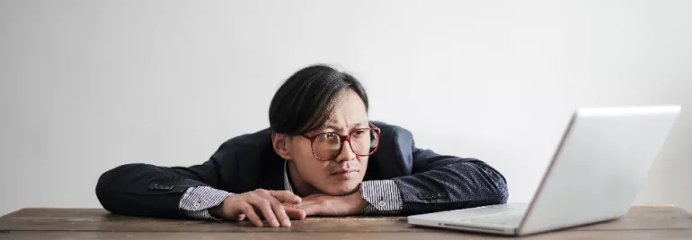 Person in glasses leaning on a table, looking at a laptop.