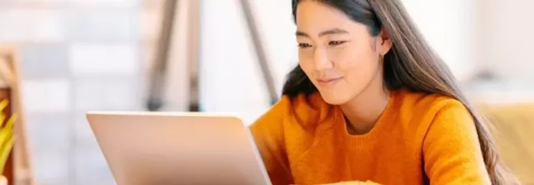 Woman in orange sweater using a laptop at home.