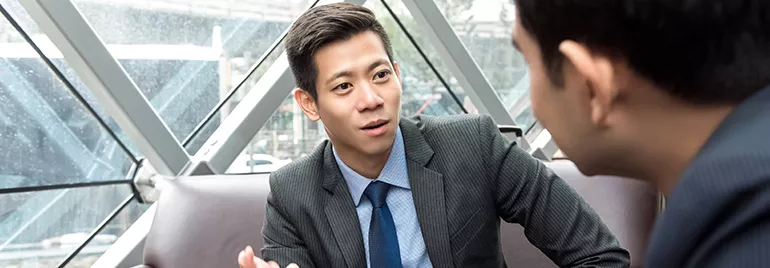 Two businessmen discussing in a modern office with large windows.