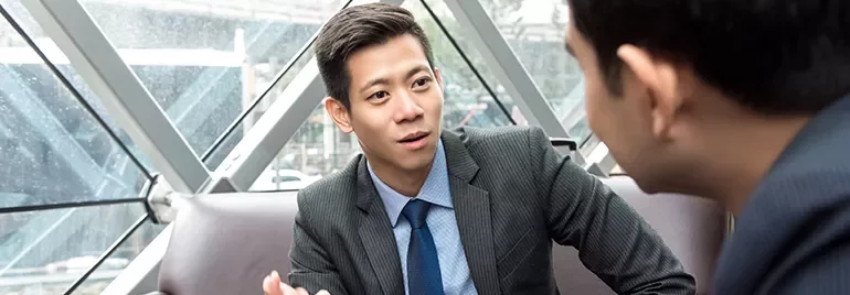 Two businessmen discussing in a modern office with large windows.