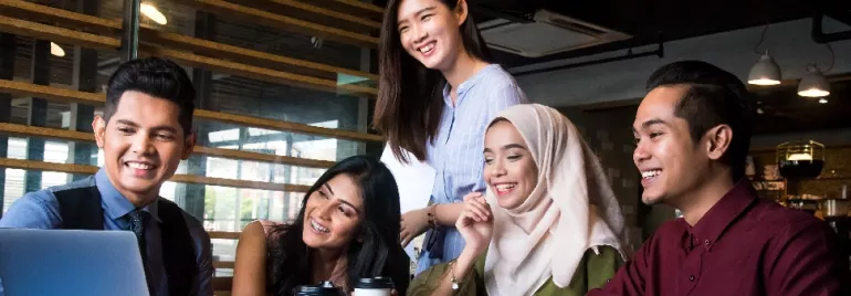 Group of five people smiling at a laptop in a modern office.