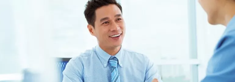Smiling man in a blue shirt talking to a colleague in an office.