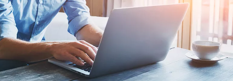 Person typing on a laptop next to a cup of coffee.