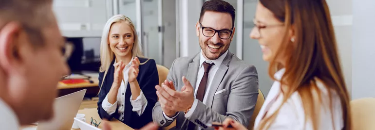Group of people in formal attire smiling and clapping at a meeting.