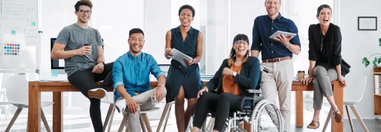 A diverse team of seven people smiling and posing in a modern office environment.