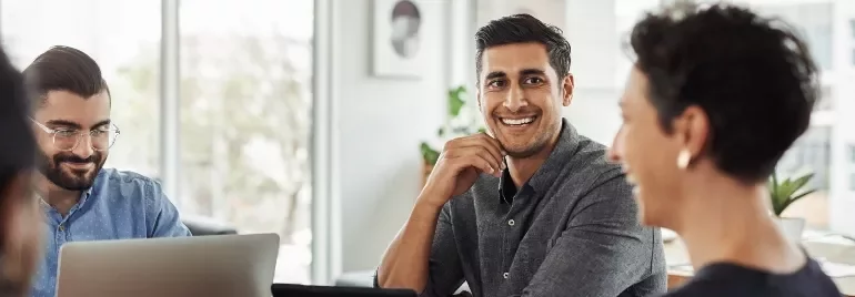 Three people smiling and working on laptops in a bright office.