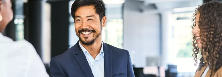 Smiling businessman shakes hands with a colleague in a bright office.