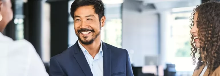 Smiling businessman shakes hands with a colleague in a bright office.