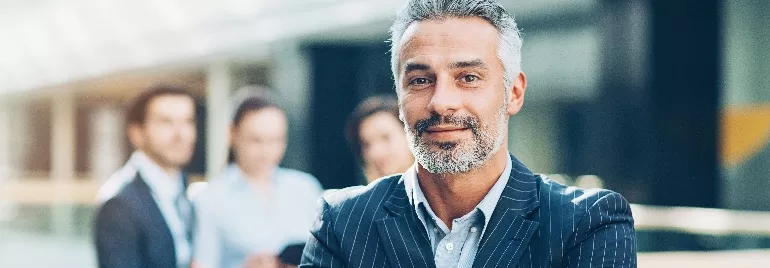 Confident man in a suit with a group of colleagues in the background.