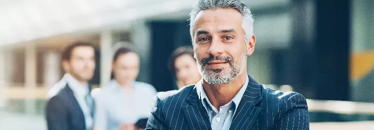 Confident man in a suit with a group of colleagues in the background.