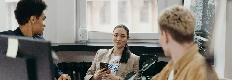 Three people in an office, one holding a phone, engaged in conversation.