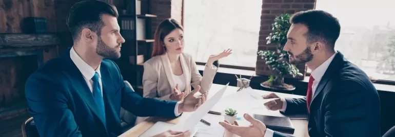 Three business professionals engaged in discussion while seated at a table
