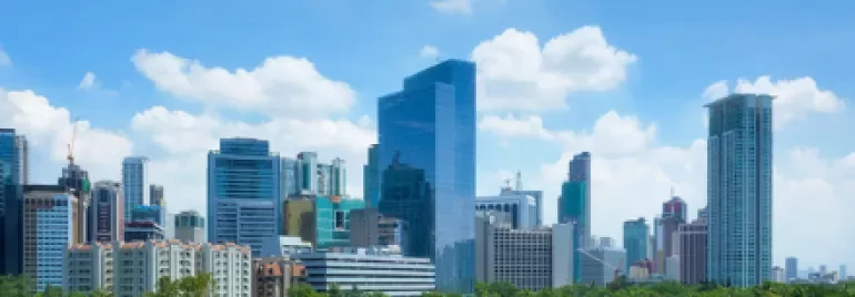 Skyline view of a city with modern skyscrapers and lush greenery under a clear blue sky.