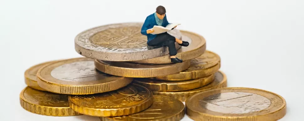Miniature figure reading on stack of coins.