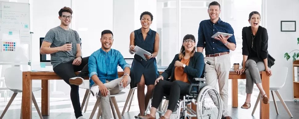 A diverse team of seven people smiling and posing in a modern office environment.