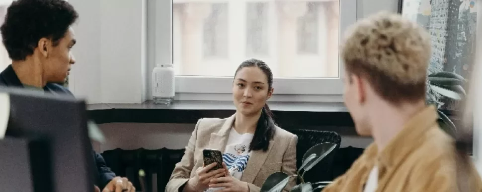 Three people in an office, one holding a phone, engaged in conversation.