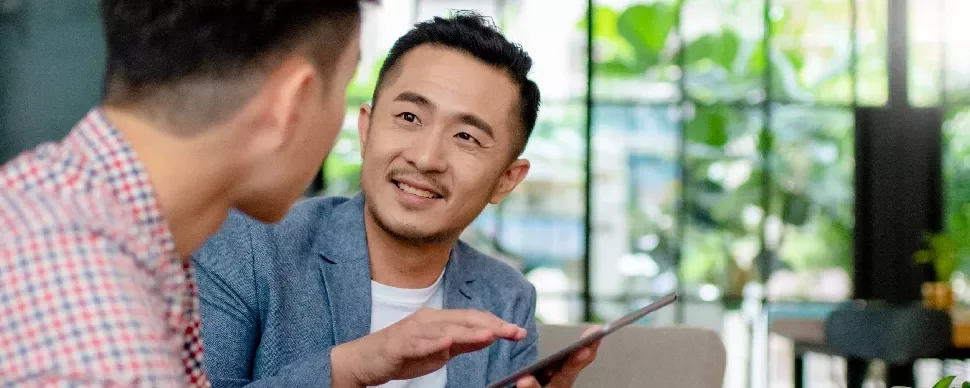One male professional holding a tablet and in discussion with another male professional