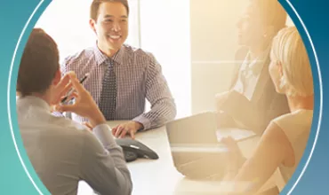 Business meeting with four people around a table, one person has a laptop.