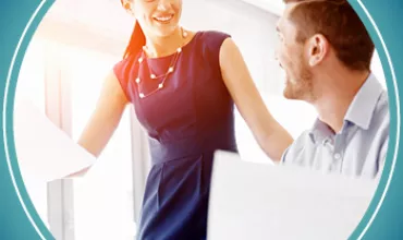 Two colleagues smiling and discussing work in a bright office.