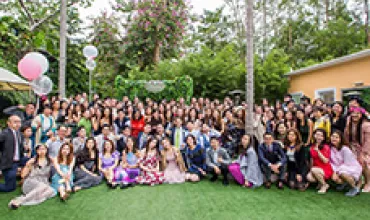 Large group of people posing in a garden, surrounded by trees and balloons.