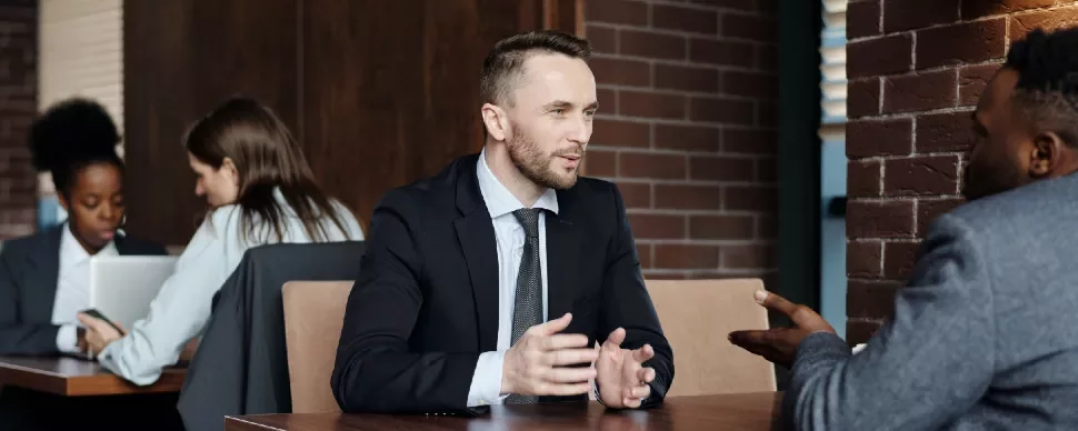Two men in suits having a discussion at a table in a coffee shop.