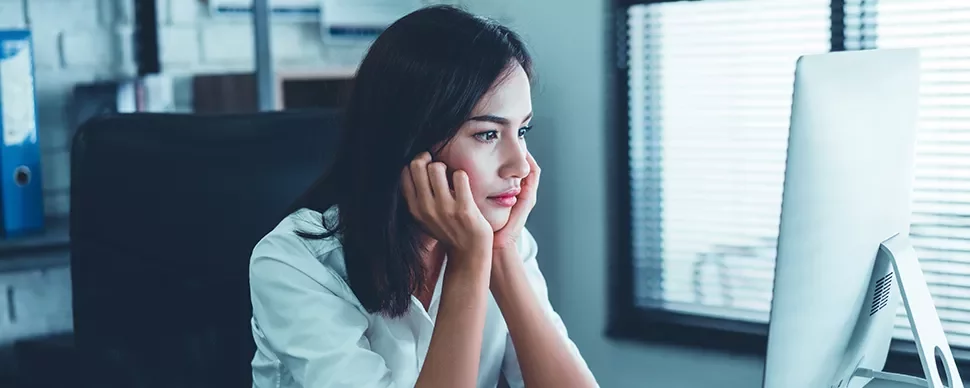 Woman in white shirt looking at computer screen with chin in hands.