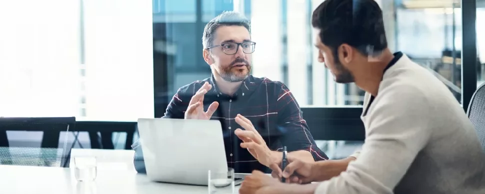 Two men having a discussion at a conference table with a laptop.