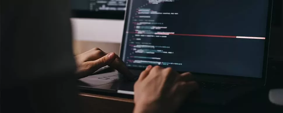 Close-up of hands typing code on a laptop in a dimly lit room.