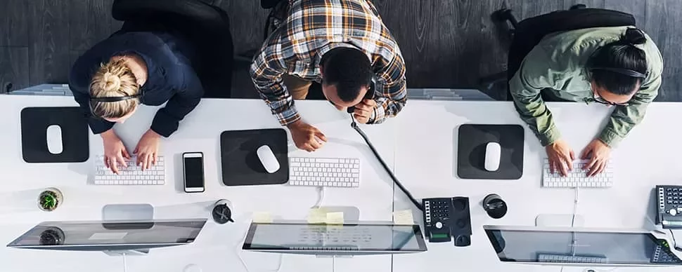 Top view of three people working at computers in an office setting.