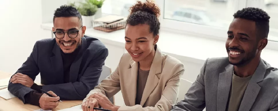 Three people sitting at a desk, smiling during a meeting.