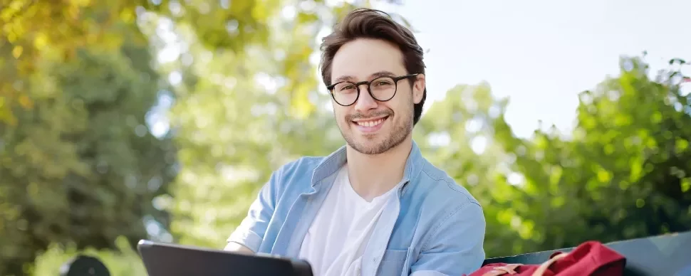 Man with glasses smiling outdoors, sitting on a bench.