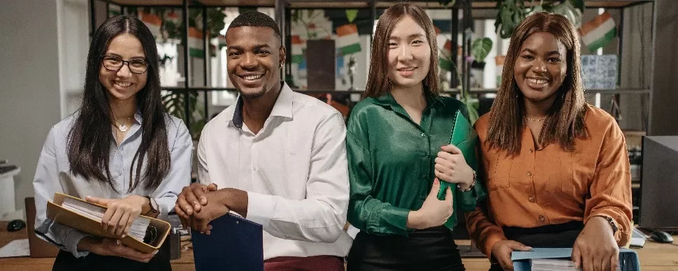 Four diverse young professionals smiling in an office setting.