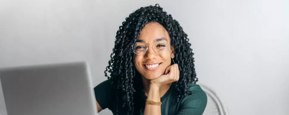 Smiling person with glasses sitting at a laptop.