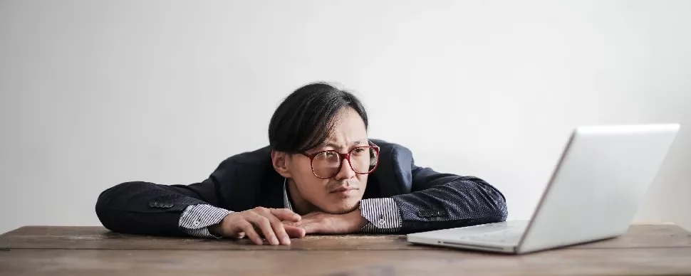 Person in glasses leaning on a table, looking at a laptop.