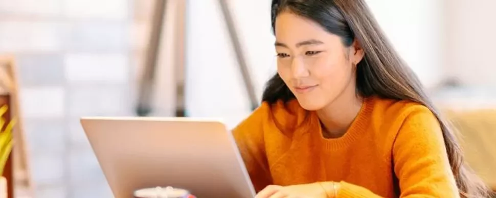 Woman in orange sweater using a laptop at home.