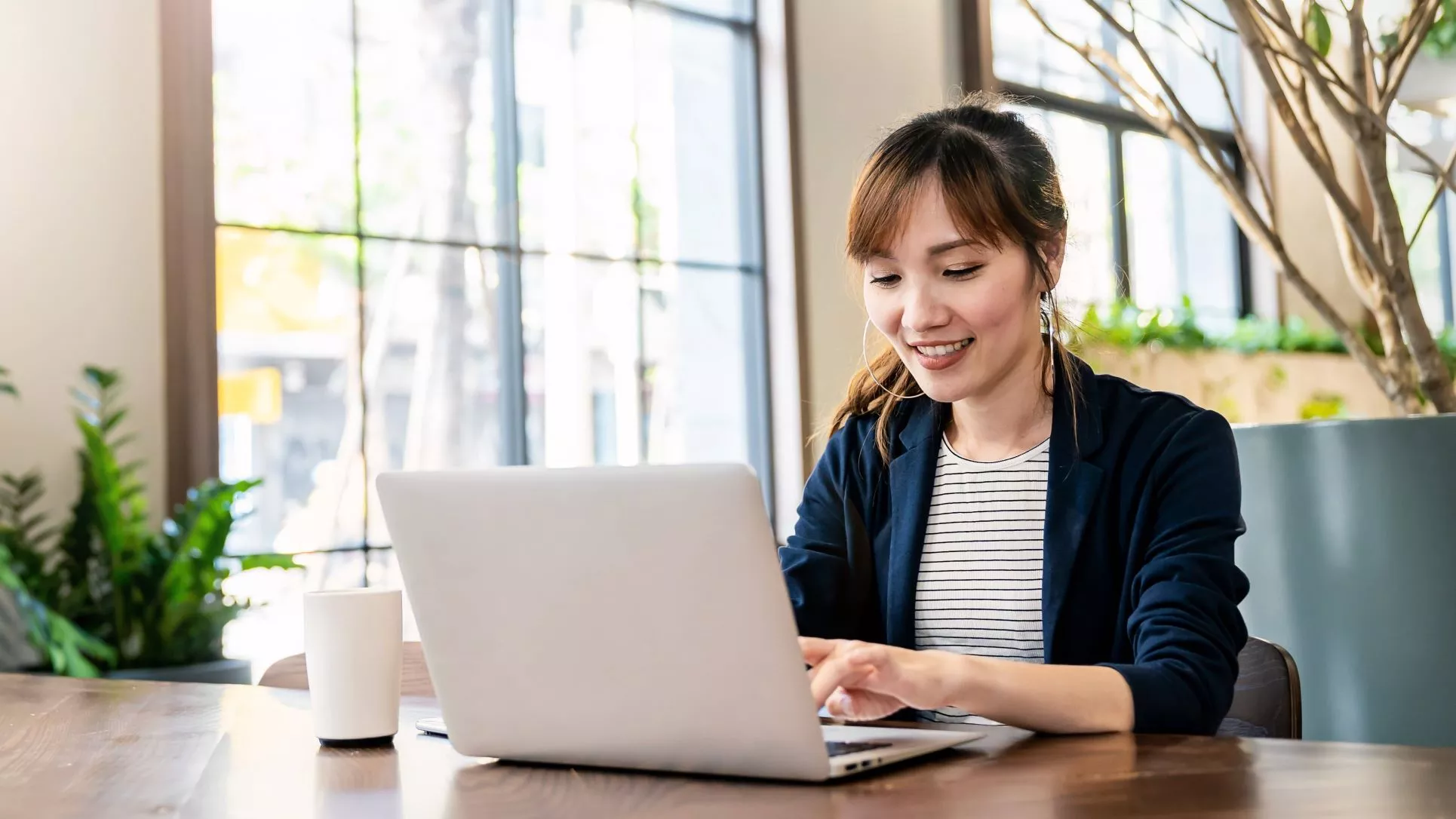 Woman smiling and working on a laptop at a wooden table.
