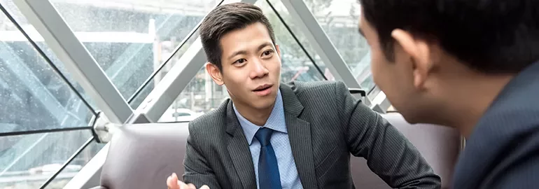 Two businessmen discussing in a modern office with large windows.