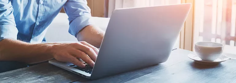Person typing on a laptop next to a cup of coffee.