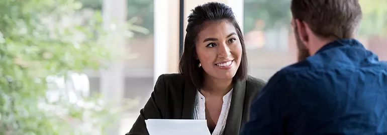 Woman in a white shirt and blazer smiling at a man with a beard during a meeting.