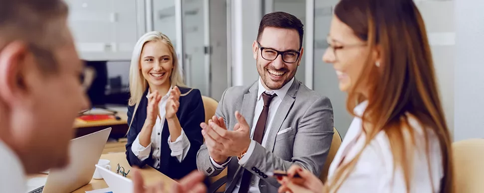 Group of people in formal attire smiling and clapping at a meeting.