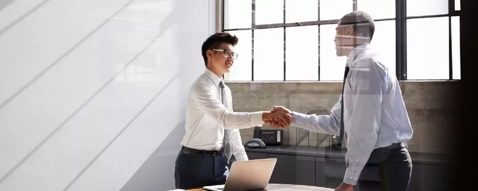 Two businessmen shaking hands in a bright office.