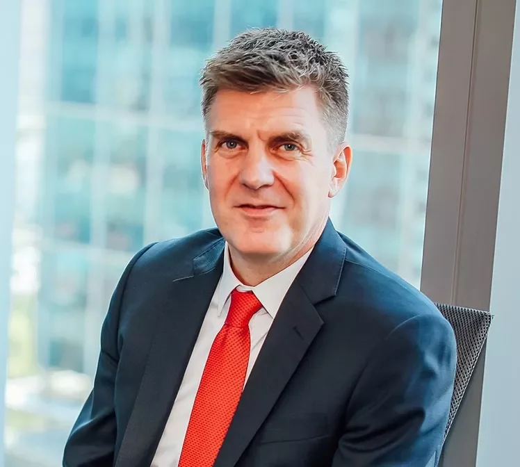 Man in a suit with a red tie sitting by a large window.
