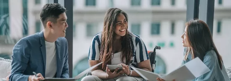 Three people having a discussion around a table in an office.